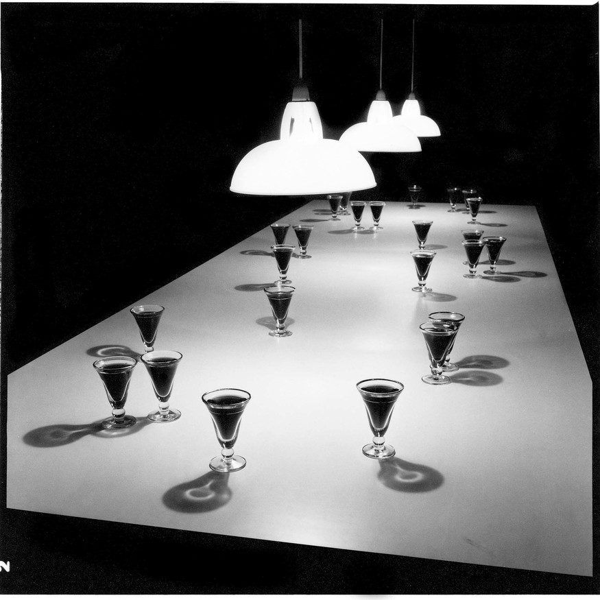 Bill Culbert Small Glass Pouring Light 1983. Serpentine Gallery, London, 1983. 25 verres bistrot, wine, Formica table, lampshades. Collection FNAC, Château d’Oiron. Photo: Bill Culbert. Reproduced courtesy Auckland University Press and the Estate of Bill and Pip Culbert
