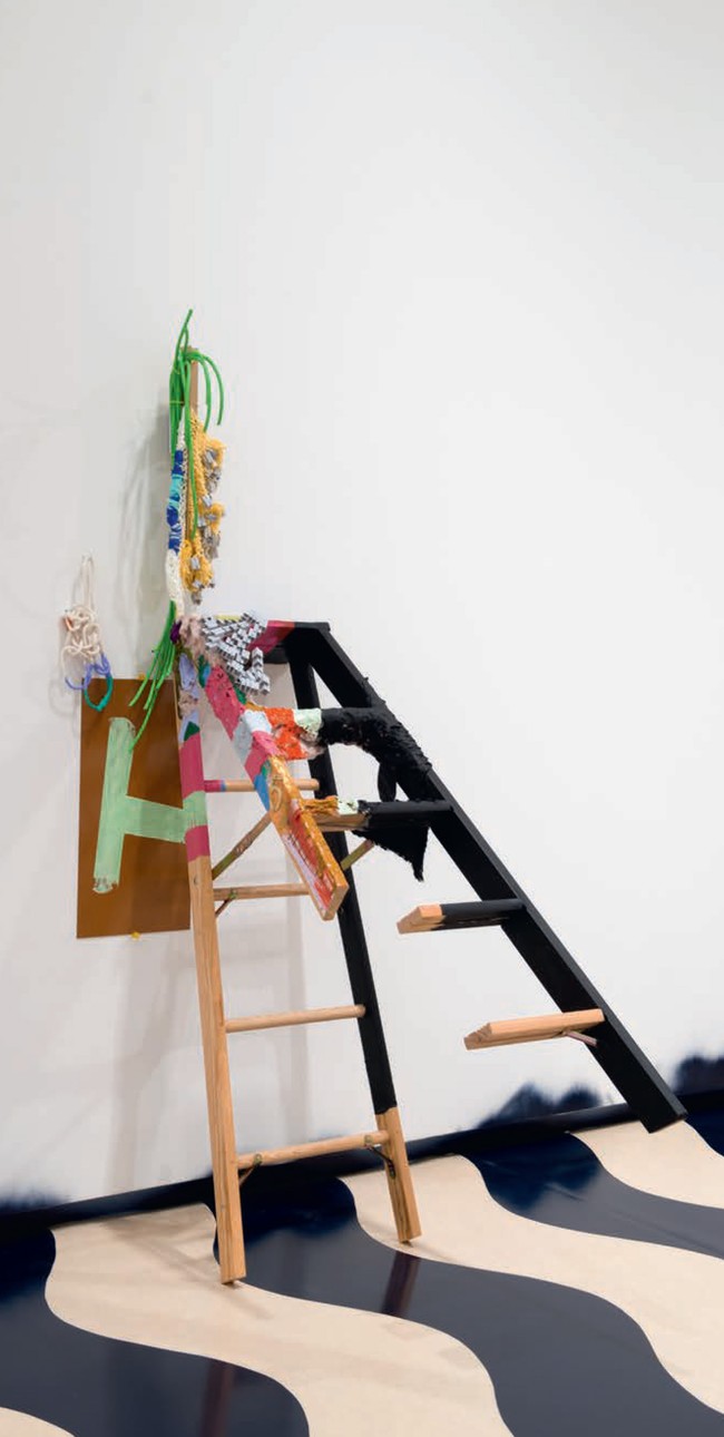 Jessica Stockholder A – H 2013. Ladder, number 5 brass, grey plastic toy modules, yard, string, green electrical cord, ochre Plexiglas, rope, acrylic paint, fake fur, cardboard angle, cable ties, TV mount, white hook, yellow tacks, 2146 x 686 x 1245 mm, installation view, A world undone, Auckland Art Gallery Toi o Tāmaki, November 2014–April 2015